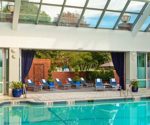 Indoor swimming pool with lounge chairs, large windows, and greenery visible outside.