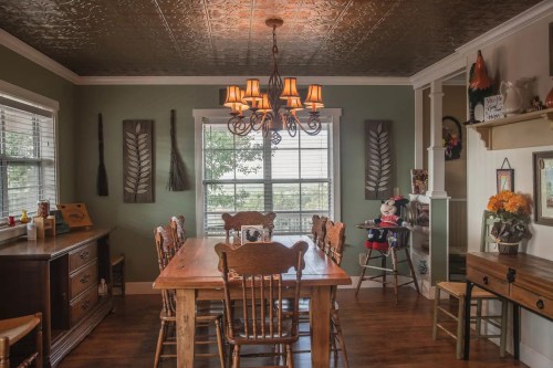 Cozy dining room with a wooden table, chairs, chandelier, and decorative wall accents, featuring a high chair in the corner.