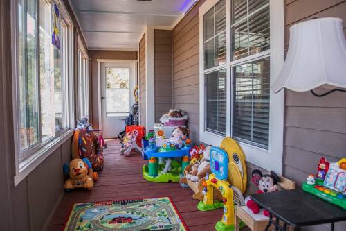 A cozy porch filled with colorful children's toys, a play mat, and a lamp, surrounded by large windows.