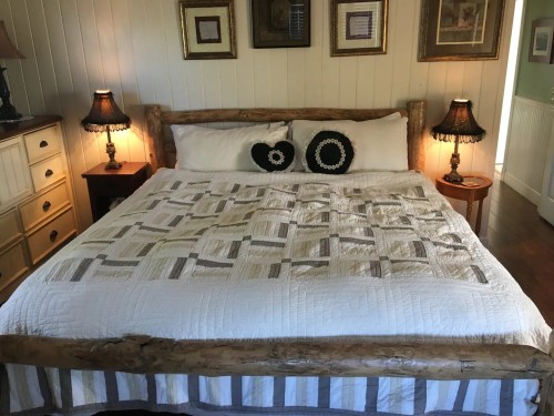 Cozy bedroom featuring a wooden bed with a quilt, decorative pillows, and lamps on bedside tables.