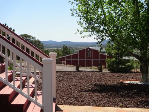 A view of a red barn in the distance, framed by trees and a staircase in the foreground, with mountains beyond.