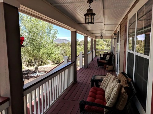 A spacious porch with comfortable seating, overlooking a green landscape and distant mountains under a clear blue sky.