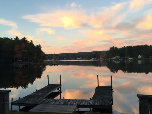 A serene lake at sunset, with colorful clouds reflecting on the water and a wooden dock in the foreground.