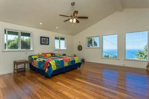 Bright bedroom with a colorful quilt, large windows showcasing ocean views, and wooden flooring.
