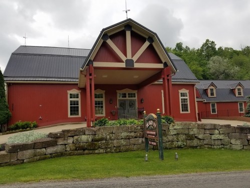 A red barn-style building with a metal roof, surrounded by greenery and stone landscaping, under a cloudy sky.