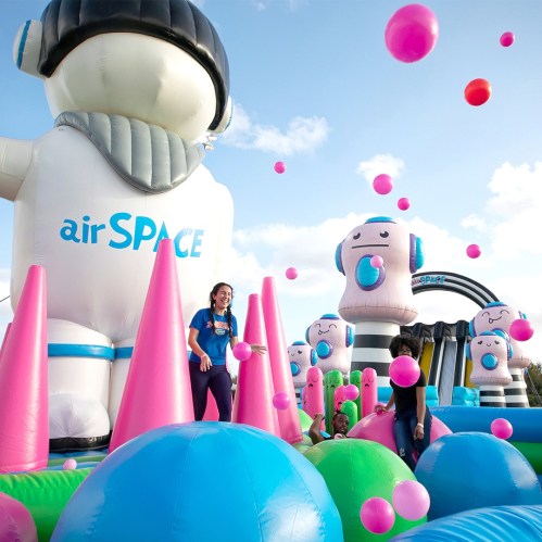 A colorful inflatable play area with large characters, balls, and children enjoying the fun under a blue sky.