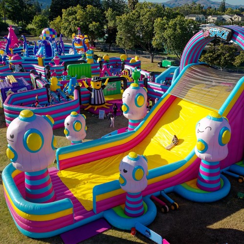 A colorful inflatable playground with slides and characters, set in a sunny outdoor space.