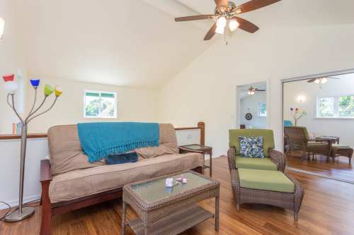 Cozy living room with a sofa, armchair, coffee table, and colorful lamp, featuring bright windows and wooden floors.