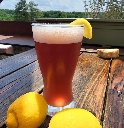 A glass of iced tea with a lemon slice, placed on a wooden table alongside two fresh lemons.