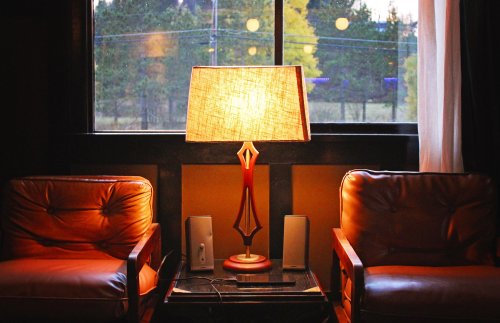 Cozy living room scene with two leather chairs, a lamp, and a window showing trees outside. Warm, inviting atmosphere.