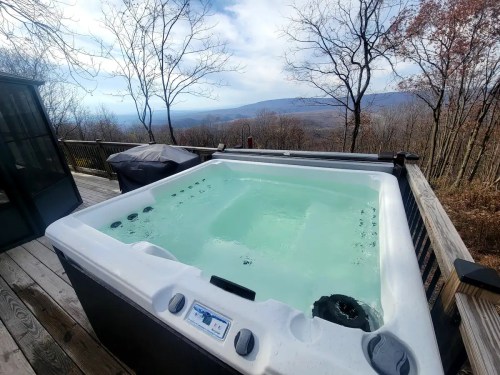 A hot tub on a wooden deck overlooking a scenic mountain view with trees in the background.