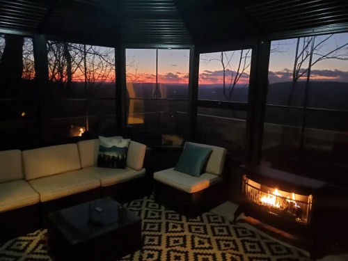 Cozy indoor seating area with a fireplace, overlooking a sunset through large windows.