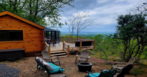 A cozy wooden cabin with a deck overlooking a scenic view, surrounded by trees and outdoor seating.