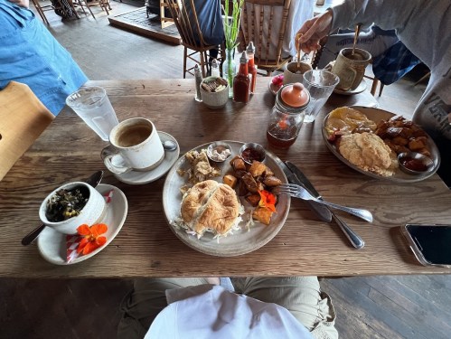 A table set with two plates of breakfast, coffee, and condiments, featuring croissants, potatoes, and fruit.