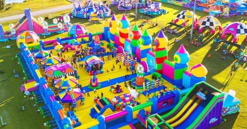 A vibrant, colorful inflatable amusement park with various slides, obstacles, and attractions filled with people.