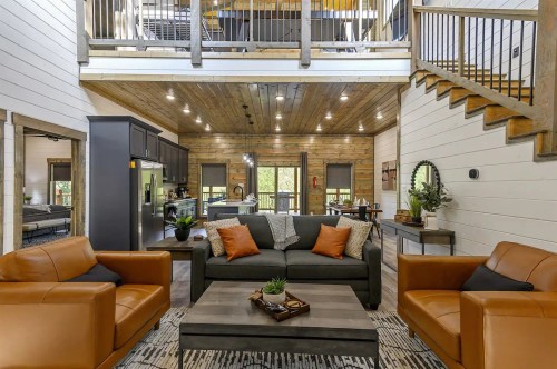 Cozy living room with a sofa, armchairs, and a wooden staircase, featuring modern decor and natural light.