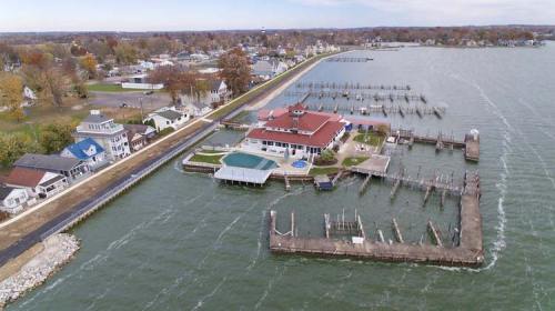 Aerial view of a waterfront area with houses, a marina, and a large building with a red roof by the water.
