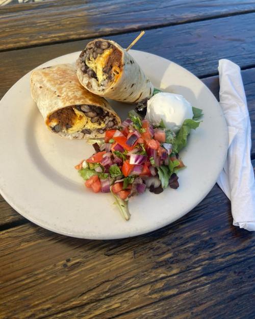 A plate with two burritos, a dollop of sour cream, and a fresh salad of tomatoes and greens on a wooden table.