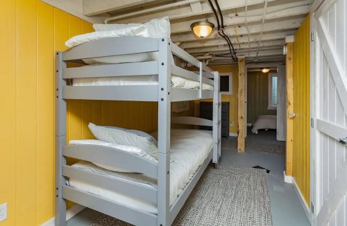 Bunk beds in a cozy, yellow-walled room with a light gray rug and wooden beams.