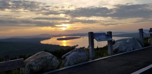 Sunset over a lake, with mountains in the background and large rocks in the foreground. Peaceful and scenic view.
