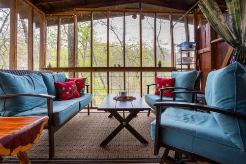 Cozy screened porch with blue seating, a wooden table, and greenery visible through the screens.
