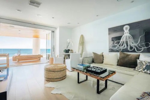 Bright, modern living room with ocean view, featuring a white sofa, coffee table, and decorative elements like an octopus artwork.