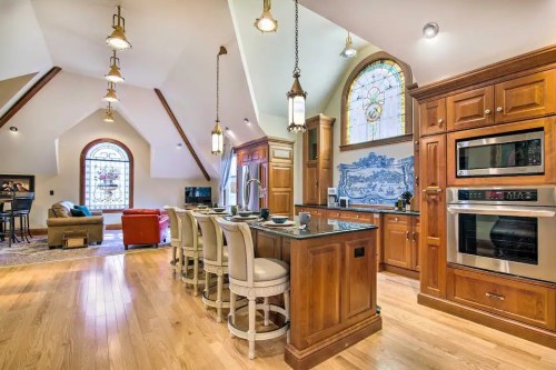 Spacious kitchen with wooden cabinets, island seating, and stained glass windows, adjacent to a cozy living area.