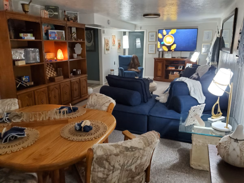 Cozy living room with blue furniture, a wooden cabinet, a TV, and a dining table set with decorative placemats.