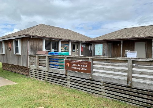 Exterior of the Ocracoke Island Discovery Center, featuring wooden architecture and a sign, set against a cloudy sky.