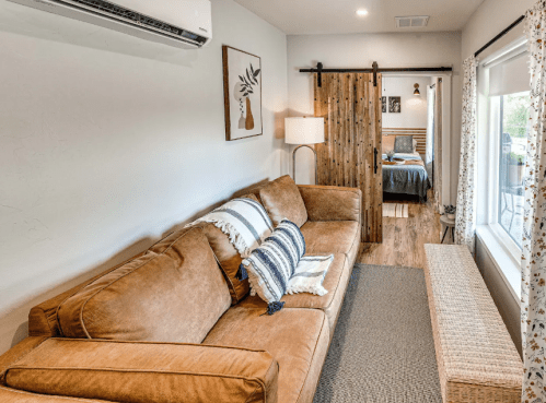 Cozy living area with a brown sofa, wooden sliding door, and a view of a bedroom in a modern, well-lit space.