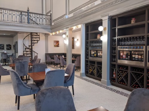 Elegant restaurant interior featuring plush chairs, wooden tables, and a wine display against a stylish backdrop.