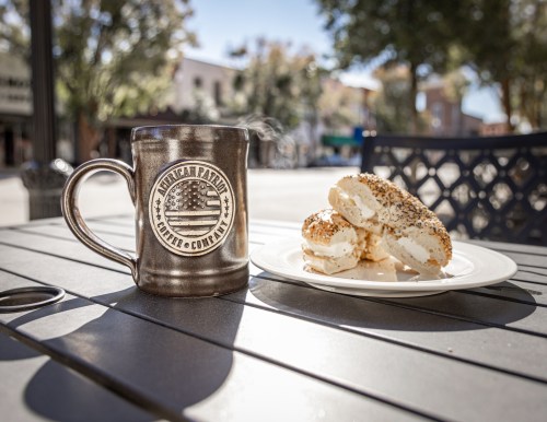 A coffee mug with an American flag design next to a plate of cream-filled pastries on a sunny outdoor table.