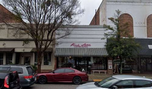 A storefront with a striped awning reading "Pink Lots" and parked cars in front, set in a small-town street.