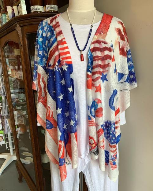 A mannequin displays a colorful, patriotic shawl featuring stars and stripes, paired with a white outfit and necklace.