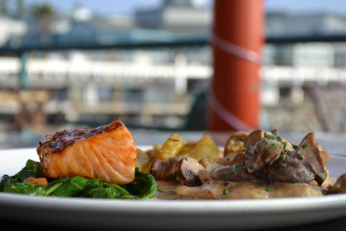 A plate featuring grilled salmon on spinach, roasted potatoes, and creamy mushrooms, with a scenic background.