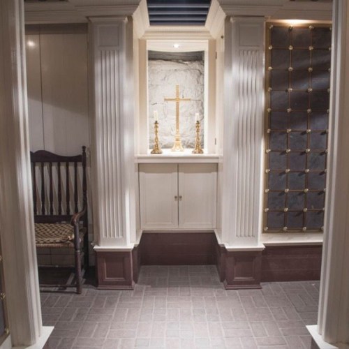 A serene interior space featuring a cross, candles, and a wooden chair, with elegant architectural details.