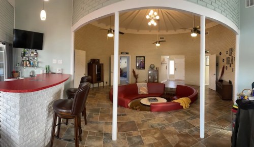 A spacious, circular room with a red seating area, bar, and light-colored walls, featuring a cozy, modern design.