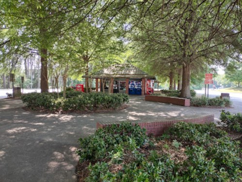 A shaded park area featuring a gazebo with vending machines surrounded by greenery and pathways.