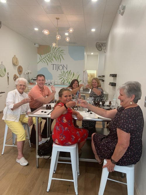 A group of six people, smiling and toasting with drinks, inside a bright, modern spa setting.