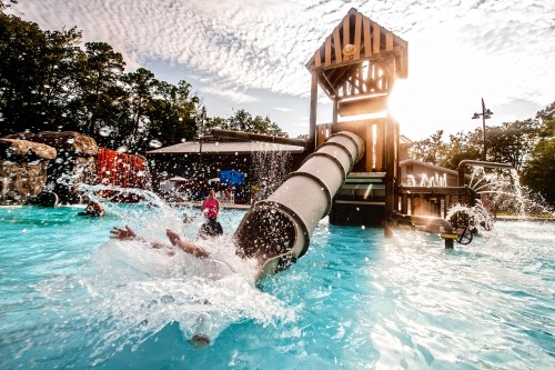A water slide at a pool with people splashing and enjoying the sunny day.