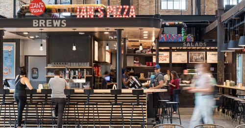 A bustling pizza restaurant with a bar, featuring a menu board and patrons enjoying food and drinks.