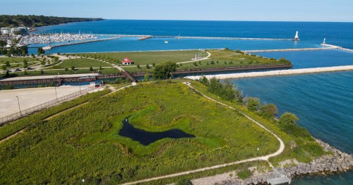 Aerial view of a coastal area with a marina, green park, and a small pond surrounded by lush vegetation.