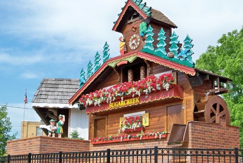 A colorful wooden building with a clock, flowers, and decorative trees, representing Sugarcreek, Ohio.