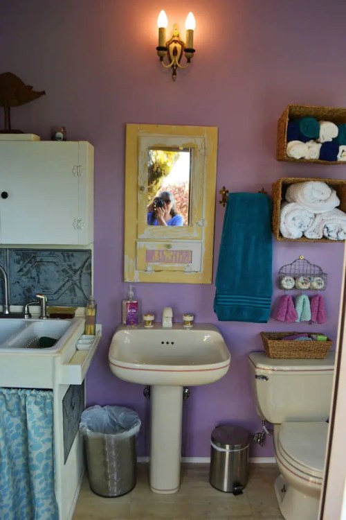 A cozy bathroom with purple walls, a sink, a mirror, towels, and decorative storage baskets.