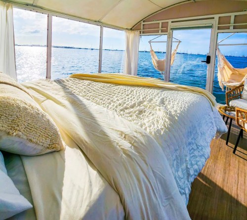 Cozy bedroom with a white quilt, overlooking a serene water view and hammocks in a bright, airy space.