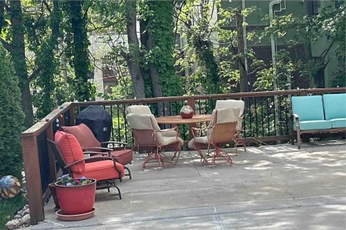 A cozy outdoor patio with a round table, chairs, and greenery in the background.