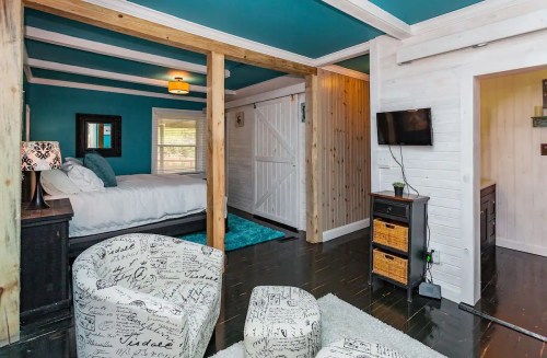 Cozy room with blue walls, wooden beams, a bed, and a small seating area featuring patterned chairs.