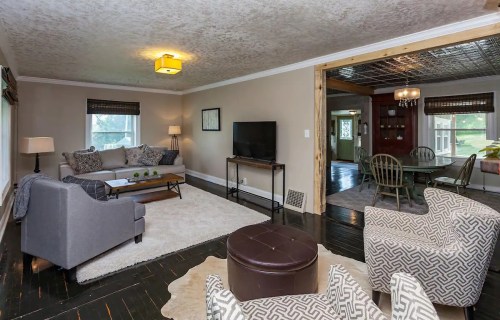Cozy living room with a gray sofa, armchairs, TV, and a dining area visible in the background. Warm, inviting decor.
