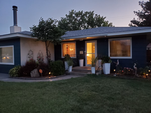 A cozy house at dusk, featuring a welcoming front porch, garden decorations, and soft lighting.