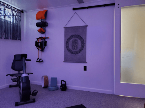 A dimly lit home gym with exercise equipment, including a stationary bike, weights, and a wall hanging.
